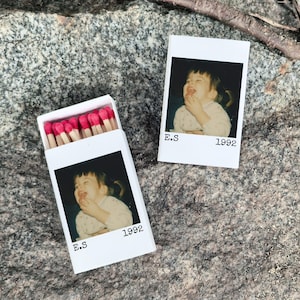 May include: White matchbox with a photo of a child eating, the text "E.S 1992" is printed below the photo. The matchbox is open, revealing red-tipped matches. A second photo with the same image and text is next to the matchbox.