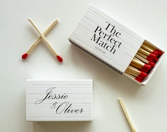 May include: White matchboxes with the text "The Perfect Match" and "12.25.26" and "Jessie & Oliver" in black script. The matches have red tips and are displayed with two crossed matches and a box of matches.