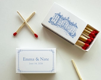 May include: White matchboxes with blue accents. One box features a detailed blue illustration of a building, while another displays the names "Emma & Nate" and the date "June 14, 2026". Several matches with red tips are visible.