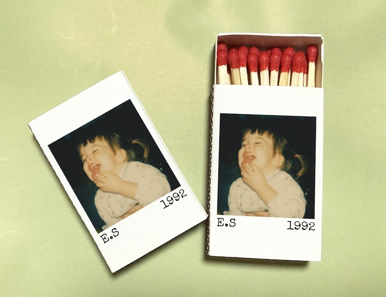 May include: A white matchbox and a Polaroid-style photo featuring a laughing child. The matchbox is open, revealing red-tipped matches. The photo and matchbox both have the text "E.S 1992".