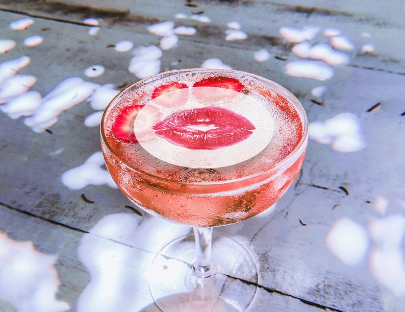May include: A pink cocktail with a lipstick kiss printed on the top. The cocktail is garnished with strawberry slices.
