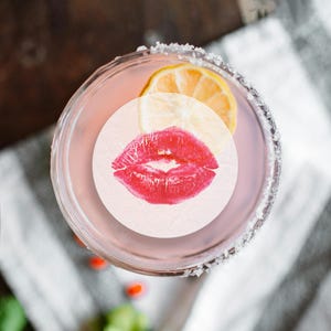May include: A pink cocktail with a lemon wedge and a red lipstick kiss on a white circle sticker.