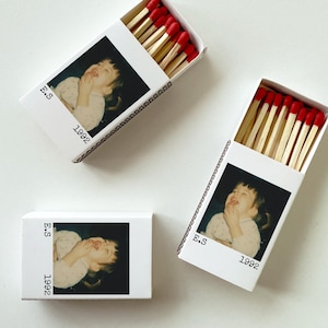 May include: Three white matchboxes, each featuring a photograph of a child. The boxes contain wooden matches with red tips. The text "E.S" and "1992" are printed on the front of each box, adding a personal touch.