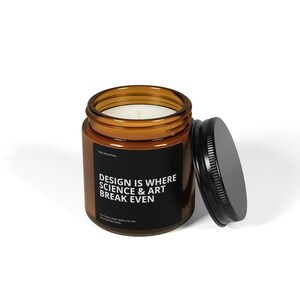 Peut inclure: Une bougie en pot de verre brun avec une étiquette noire et un couvercle noir. L'étiquette indique "DESIGN IS WHERE SCIENCE & ART BREAK EVEN". La bougie est remplie de cire blanche et a une seule mèche.