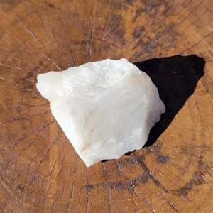 May include: A large, white, rough-hewn quartz crystal on a wooden surface.