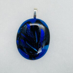 May include: A blue and black glass pendant with a silver bail. The glass has a swirling pattern and a glossy finish.