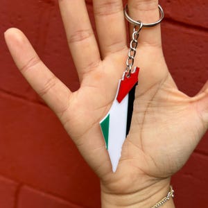 May include: A keychain in the shape of a country, with a flag design in red, white, green, and black. The keychain is attached to a silver metal ring and chain.