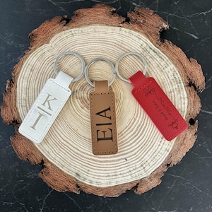 May include: Three leather keyrings in white, brown, and red, each with a silver ring. The white keyring has the letter "K" engraved, the brown keyring has "EIA", and the red keyring has the text "Sweet & Salty".