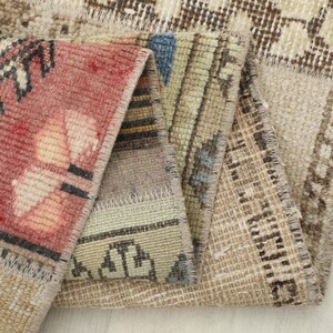 Op de afbeelding: Close-up van een opgevouwen, veelkleurig tapijt. Het tapijt heeft een patchwork-ontwerp met verschillende patronen en kleuren, waaronder rood, beige, blauw en bruin. De randen zijn netjes afgewerkt en tonen de constructie en textuur van het tapijt.