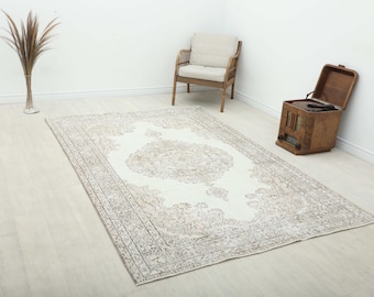 May include: A rectangular area rug featuring a cream-colored center with a large, intricate medallion pattern in muted brown and beige tones. The rug has a wide, detailed border with repeating floral and geometric motifs in matching neutral colors.