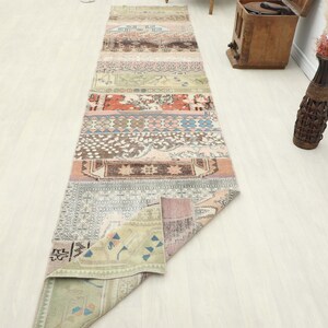 Peut inclure: Un long tapis rectangulaire en patchwork avec une variété de motifs et de couleurs, dont le beige, le rose, le bleu et le vert. Le tapis est composé de plusieurs pièces rectangulaires cousues ensemble, créant un design unique. Le tapis est sur un sol en bois clair.