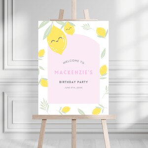 May include: A welcome sign for a birthday party with a pink background and lemons with smiling faces. The text reads "Welcome to Mackenzie's Birthday Party June 5th, 20XX".