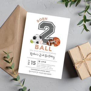 May include: A white invitation with a gray number "2" and the words "Born 2 Ball" in a brown font. The number is decorated with a soccer ball, baseball, and football. The invitation is for a 2nd birthday party and includes the date, time, and location.