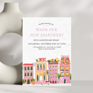 May include: A housewarming party invitation with a pink and orange illustration of a row of colorful houses with a small car in front. The text reads "You're invited to Warm Our New Apartment with laughter and drinks. Saturday, October 21st at 5 PM. 123 anywhere st., Any City, st 12345. RSVP to 533.455.6767."