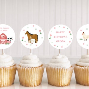 May include: Four cupcakes with farm animal themed cupcake toppers. The toppers are round and feature a horse, a barn with a cow, pig, and sheep, a chicken, and the text "OINK, CLUCK, BAA, MOO..." and "HAPPY BIRTHDAY OLIVIA".