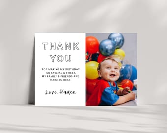 May include: A white thank you card with black text that reads "THANK YOU" and "FOR MAKING MY BIRTHDAY SO SPECIAL & SWEET, MY FAMILY & FRIENDS ARE HARD TO BEAT! Love. Kaden". The card has a photo of a baby boy wearing a red and blue superhero costume and surrounded by colorful balloons.