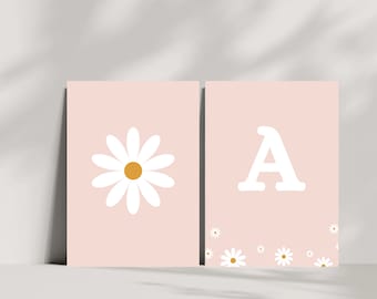 May include: Two pink printable wall art prints with a white daisy on one and the letter A on the other. Both prints have small white daisies scattered at the bottom.