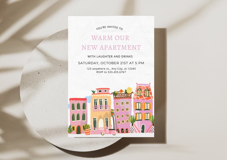 May include: A housewarming party invitation with a colorful illustration of a row of houses with pink, yellow, and red accents. The text reads "You're invited to Warm Our New Apartment with laughter and drinks. Saturday, October 21st at 5 PM. 123 anywhere st., Any City, st 12345. RSVP to 533.455.6767."