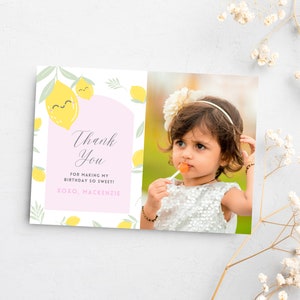 May include: A pink and white thank you card with a lemon theme. The card has a photo of a young girl with a flower headband and a lollipop. The text on the card reads "Thank You for making my birthday so sweet! xoxo, Mackenzie".