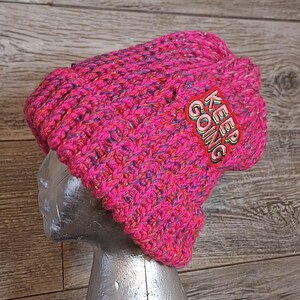 May include: Pink and purple knitted beanie with a sparkly finish and a red and yellow patch that says "KEEP GOING".