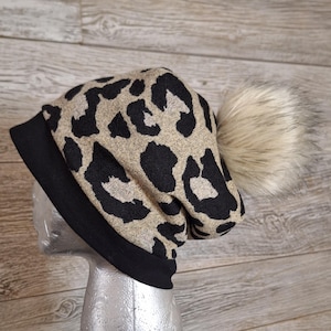 May include: A black and tan leopard print beanie with a black fold-over brim and a fluffy white pom pom.