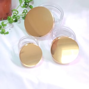 May include: Three clear glass jars with gold lids. The lids are round and have a shiny finish. The jars are different sizes.