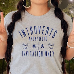 May include: A light grey athletic heather t-shirt with the words "Introverts Anonymous" in dark blue. The shirt also features the phrases "Don't Call, Don't Text, Invitation Only" in dark blue. The t-shirt is made of a soft, comfortable material.