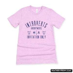 May include: A lilac t-shirt featuring the navy blue text "Introverts Anonymous". The design includes the phrases "Don't Call, Invitation Only, Don't Text". The shirt is made of a soft material.