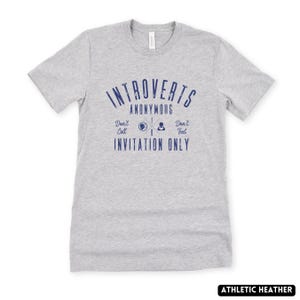 May include: A grey athletic heather t-shirt with the blue text "Introverts Anonymous". The shirt also has the phrases "Don't Call, Don't Text, Invitation Only" in blue. The t-shirt is a crew neck style.