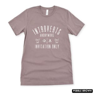 May include: Pebble brown t-shirt featuring the white text "Introverts Anonymous". Below, the shirt reads "Don't Call, Invitation Only, Don't Text". The t-shirt is a crew neck style and is made of a soft material.