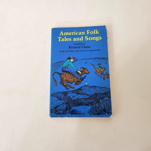 May include: A vintage book titled "American Folk Tales and Songs" by Richard Chase. The cover is blue with illustrations of people riding animals. The text includes "Songs with Music and Guitar Accompaniment".