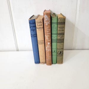 May include: A collection of vintage books with colorful spines. Titles include "Heidi Grows Up," "Little Lord Fauntleroy," and "The Little Girl." The books are arranged on a white surface, showcasing their aged covers and classic design.