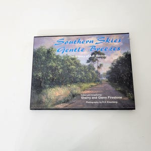 May include: A framed print titled "Southern Skies Gentle Breezes" featuring a landscape painting. The artwork depicts a road through a tree-lined area under a blue sky. The text "The Artistry of A.E. Backus" is also visible.