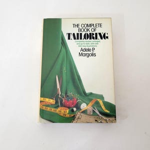 May include: The Complete Book of Tailoring by Adele P. Margolis. The book cover features a green fabric draped over a table with sewing supplies, including scissors, pins, thread, and a measuring tape.