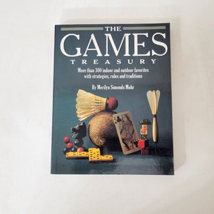 May include: A book titled "THE GAMES TREASURY" with various game pieces arranged on the cover. The cover features a badminton shuttlecock, playing card, chess piece, dominoes, and a dart. The book promises over 300 indoor and outdoor games.
