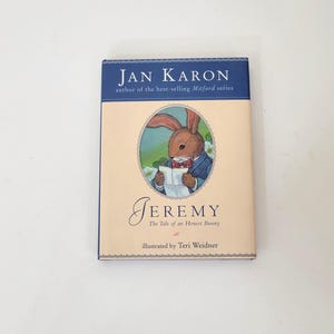 May include: A hardcover book titled "Jeremy: The Tale of an Honest Bunny" by Jan Karon. The cover features an illustration of a brown rabbit wearing a suit and reading a paper. The book has a blue border with the author's name.