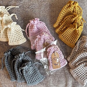 May include: Assortment of crocheted drawstring bags in various colours, including beige, grey, and pink. The bags are made with a delicate stitch pattern and have a simple, elegant design.