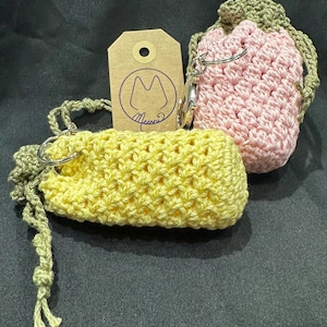 May include: Two crocheted drawstring bags with a key ring. The bag on the left is yellow and the bag on the right is pink. The bags are handmade and have a rustic, vintage look.