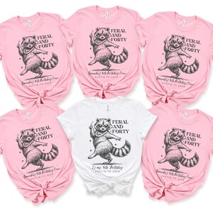 Puede incluir: Varias camisetas rosas y blancas con un dise&ntilde;o de mapache. El mapache lleva un collar de perlas y el texto "FERAL AND FORTY" est&aacute; encima. Debajo est&aacute; el texto "Amanda's 40th Birthday Crew, Austin TX 2026" o "It's my 40th Birthday, Austin TX 2026".