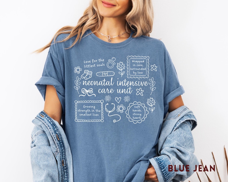 Op de afbeelding: Blauw spijkerbroekkleurig T-shirt met witte tekst en illustraties over neonatale intensive care. Het shirt bevat zinnen als "Love for the littlest souls" en "Growing strength in the smallest lives."
