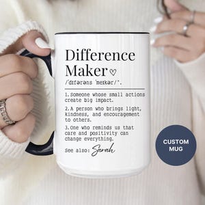 May include: White ceramic mug with a black handle and rim, featuring the text "Difference Maker" and its phonetic pronunciation. The mug includes definitions and the name "Sarah". A navy blue circle with "CUSTOM MUG" is on the side.
