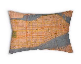 May include: Rectangular pillow featuring a vintage map of New York City. The map is in shades of yellow, orange, and blue, with detailed street grids and geographical features. The pillow has a soft, textured appearance, suggesting a comfortable home decor item.