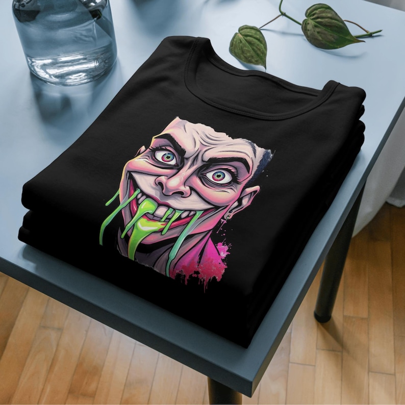 May include: Black t-shirt with a graphic print of a cartoon character with green slime dripping from its mouth. The character has a pink and purple background.