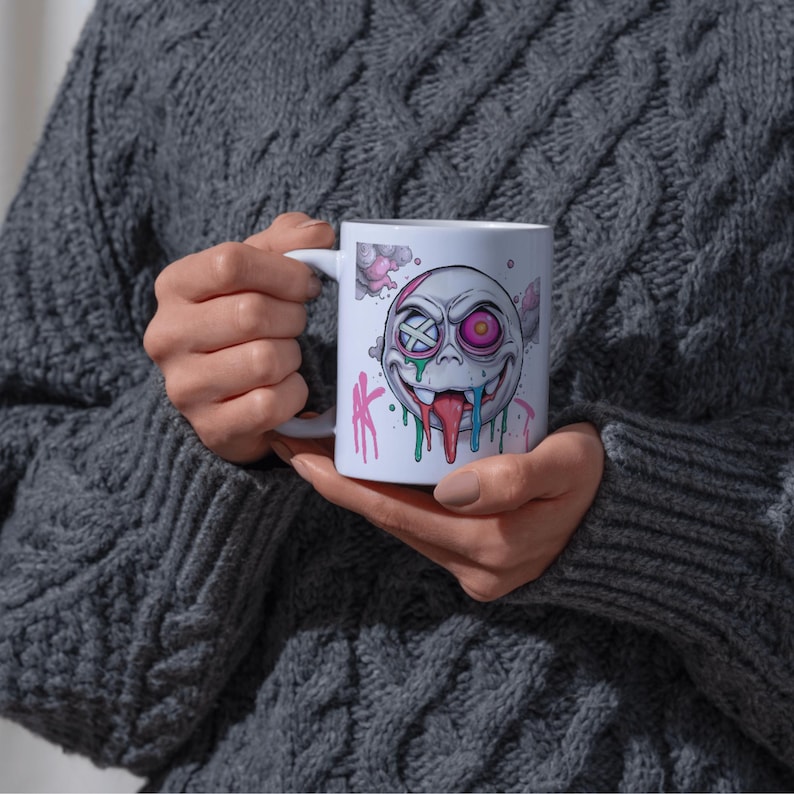 May include: White ceramic mug with a colorful cartoon face with one eye covered by a bandage and a dripping tongue. The face is surrounded by pink, blue, and green splatters.