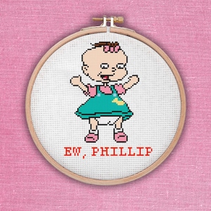 Puede incluir: Aro de bordado de punto de cruz con una imagen de dibujos animados de una niña pequeña con un vestido azul y un lazo rosa. El texto "EW, PHILLIP" está bordado debajo de la imagen.
