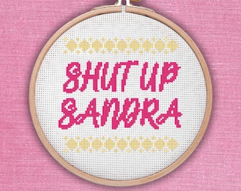 Könnte beinhalten: Ein weißer Stickrahmen mit einem pinkfarbenen und gelben Kreuzstich-Design, auf dem "SHUT UP SANDRA" steht.