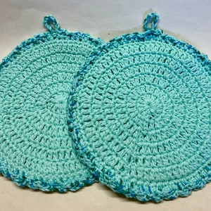 May include: Two crocheted pot holders in a light blue and teal color scheme. The pot holders are round and have a crocheted border.