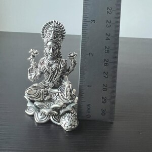 Op de afbeelding: Zilveren beeld van de hindoegodin Lakshmi zittend op een lotusbloem. Ze houdt een lotusbloem in elke hand en draagt een kroon op haar hoofd. Het beeld is ongeveer 15 cm hoog.