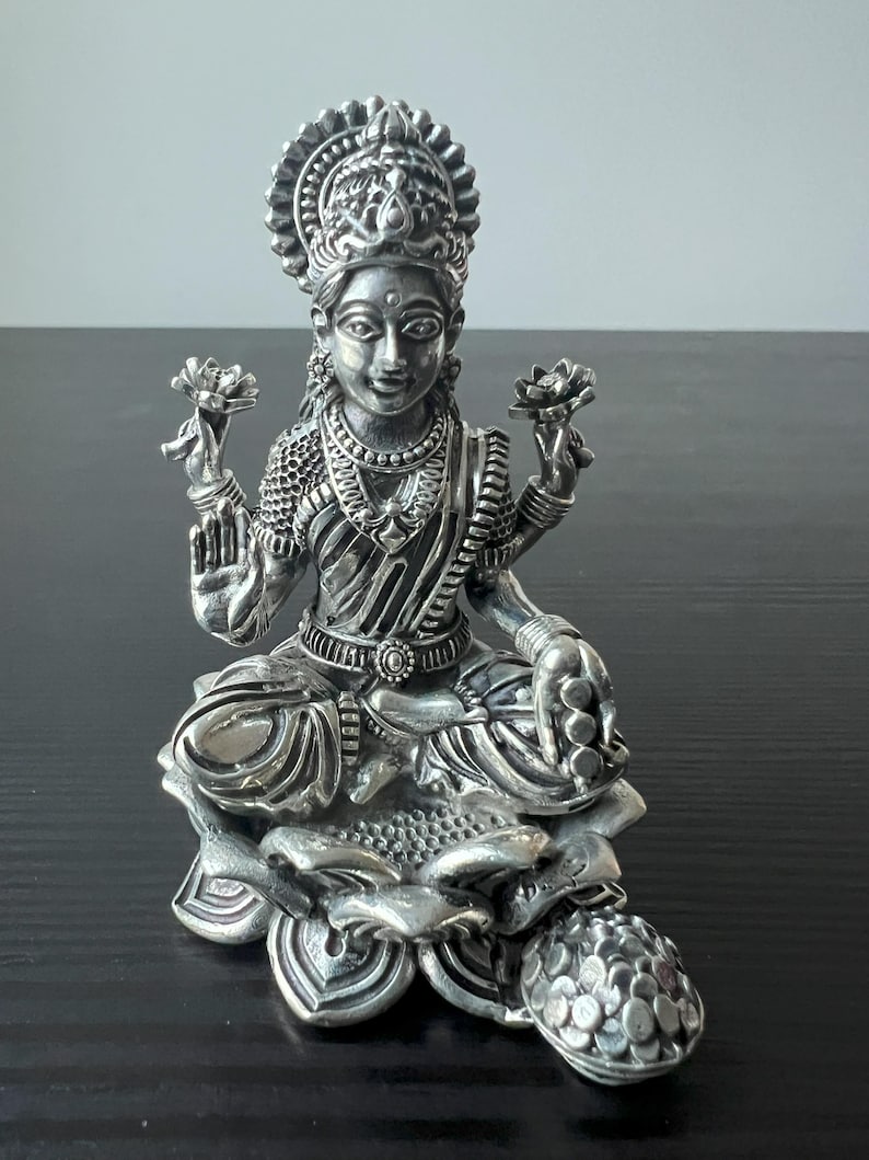 Op de afbeelding: Een zilveren beeld van de hindoegodin Lakshmi, zittend op een lotusbloem. Ze houdt een lotusbloem in elke hand en heeft een serene uitdrukking op haar gezicht.