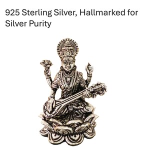 May include: A silver statue of a deity, seated on a lotus flower, playing a stringed instrument. The statue is intricately detailed and hallmarked for silver purity.